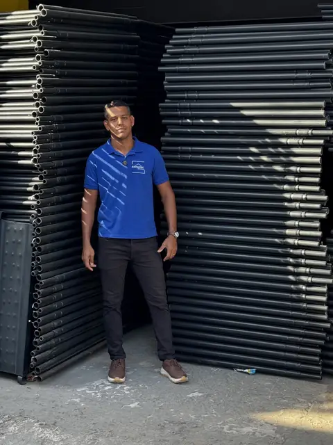 Pessoa da nossa equipe, de camisa azul, entre pilhas de painéis de andaime no galpão